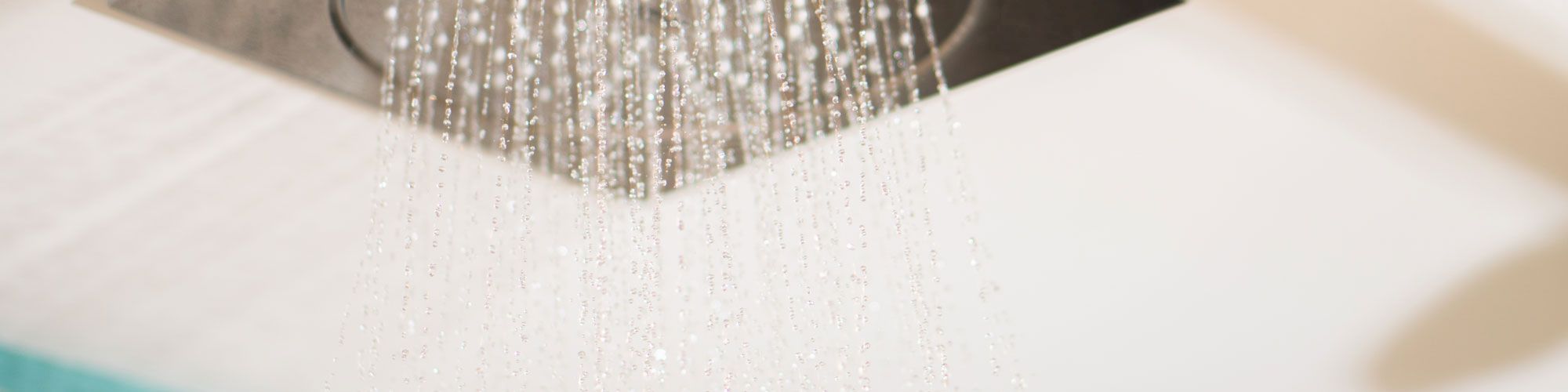 The image shows a ceiling-mounted square showerhead with water flowing, indicating a running shower in what appears to be a modern bathroom.