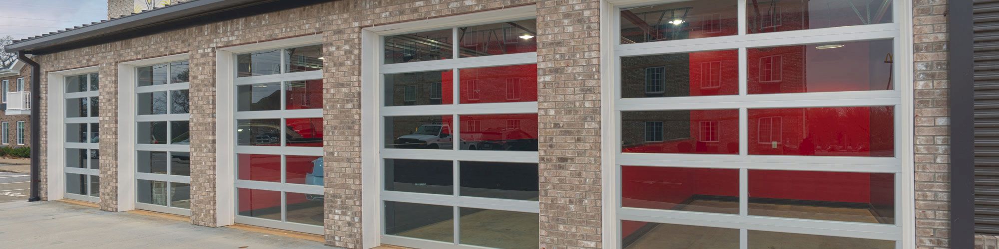 The image shows a building with four large glass paneled garage doors, likely part of a commercial structure or residential complex, with balconies above.