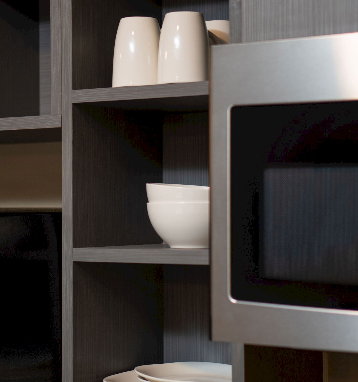 The image shows a kitchen with open shelves holding white bowls, plates, and cups, along with a microwave oven built into the cabinetry.