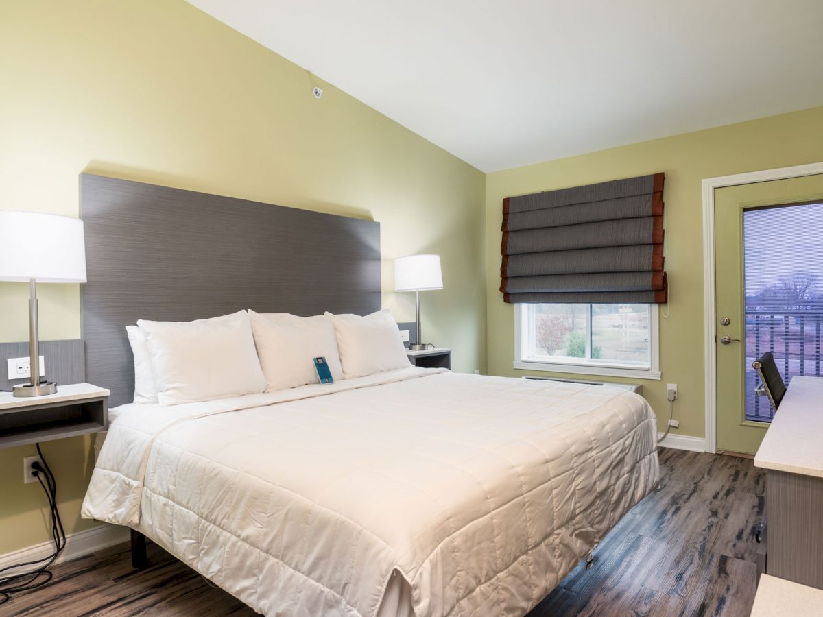 A cozy bedroom with a large bed, bedside tables with lamps, a window with blinds, and a door leading outside.