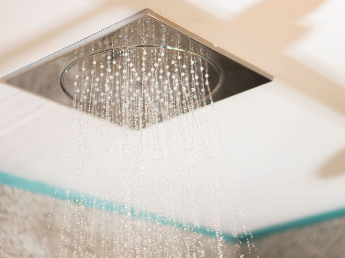 The image shows a ceiling-mounted, square-shaped rain showerhead with water streaming down, likely in a modern bathroom setting.