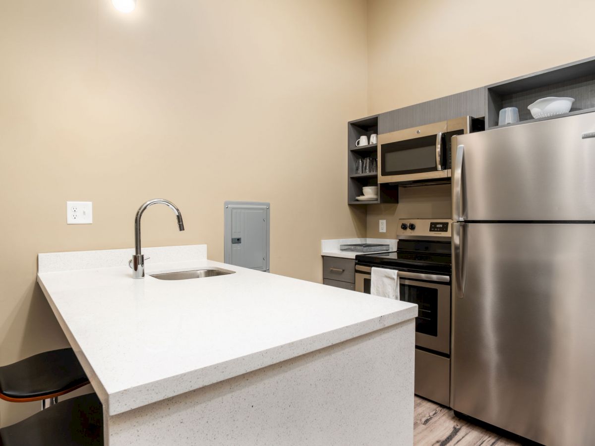 A modern kitchen with a refrigerator, microwave, and oven. It has a sink and countertop, along with a couple of chairs for seating.