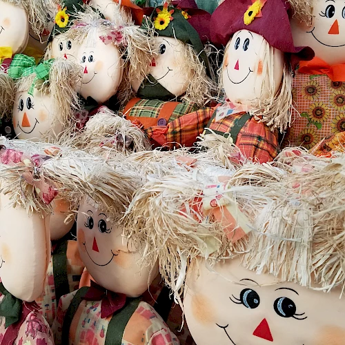 The image shows a collection of cheerful scarecrow dolls with straw hair and colorful clothes, featuring bright, happy faces in close arrangement.
