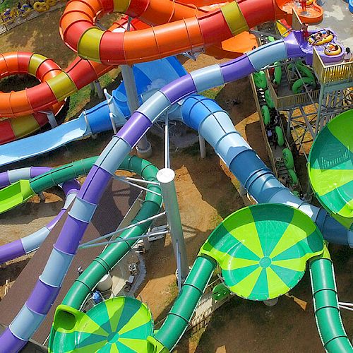 This image shows a vibrant water park with multiple colorful water slides, splash pools, and tubes. People can be seen enjoying the attractions.