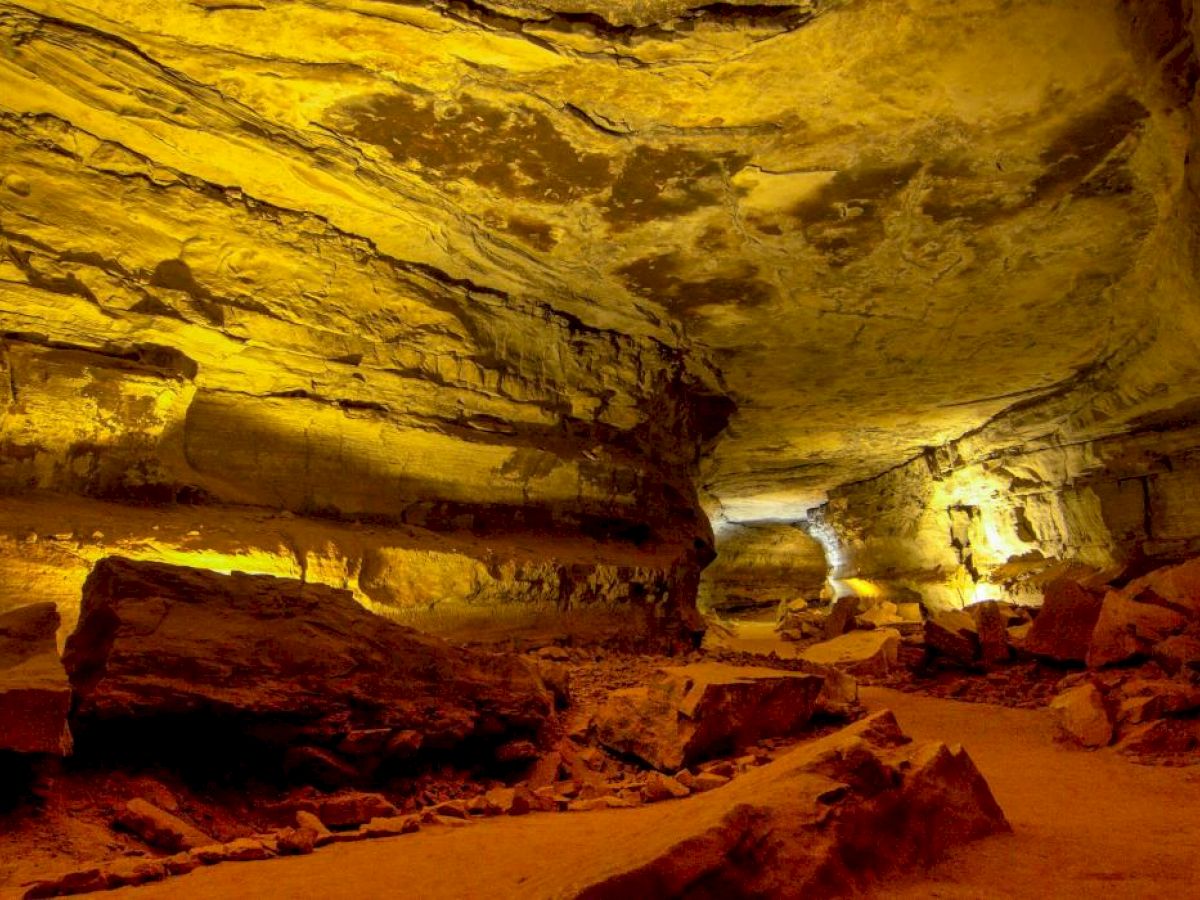 The image depicts an illuminated cave interior with rocky formations and a rough, uneven floor. The lighting creates a warm, golden glow.