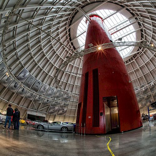 A fisheye view of an indoor car museum with a tall red structure in the center and various cars displayed around.