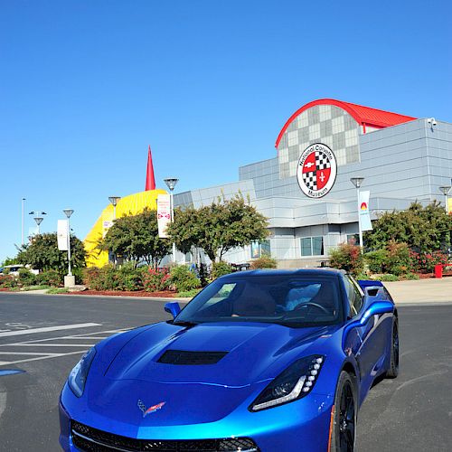 A blue sports car is parked in front of a building with a large red and white logo on its facade, under a clear blue sky.