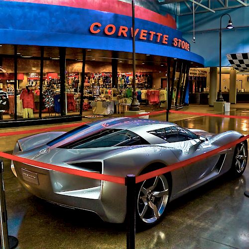 The image features a silver sports car on display, roped off in front of a store with a sign that reads 