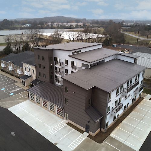 An aerial view of a multi-story building in an industrial area with adjacent parking lots and surrounding structures under a cloudy sky.