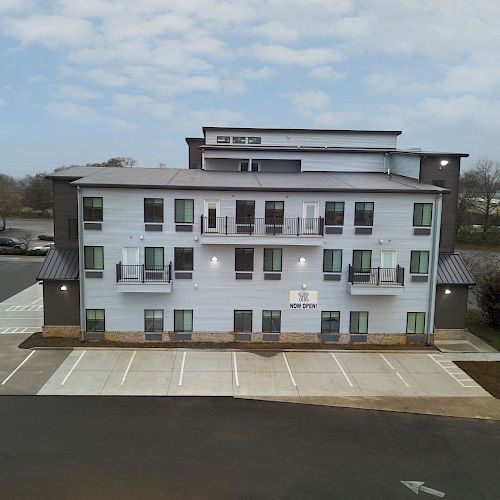 A multi-story building with a small parking lot in front and several parking spaces, surrounded by other structures and a few parked cars.