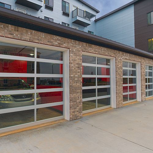 This image shows a row of modern garage doors integrated into a building, with one door partially open, revealing a parked car inside.