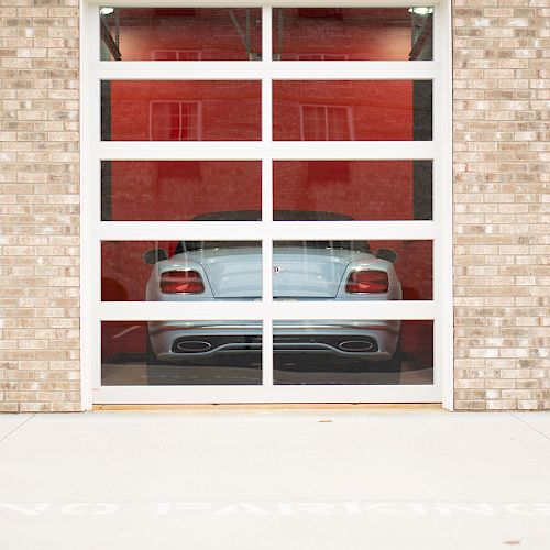 A luxury sports car is parked behind a glass garage door with a 