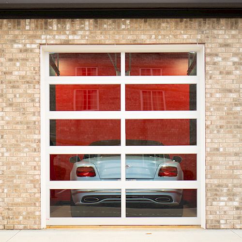 The image shows a sports car behind a glass garage door in a brick building, with 