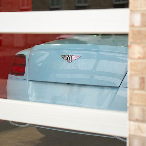 A luxury car is partially visible through a glass garage door. The emblem indicates the brand, and the car is parked inside a building.