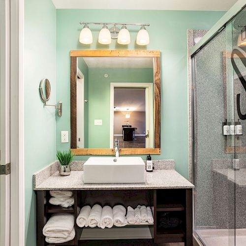 A bathroom with a sink, mirror, towels, and toiletries; shower with glass door on the right and toilet on the left.