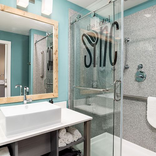 A modern bathroom with a large mirror, a white sink, and a glass shower. The shower has text on it and toiletries on the wall.