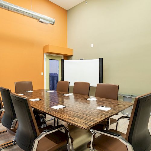 A modern conference room with an orange accent wall, a large table, eight chairs, a whiteboard, and a projector screen is displayed in the image.