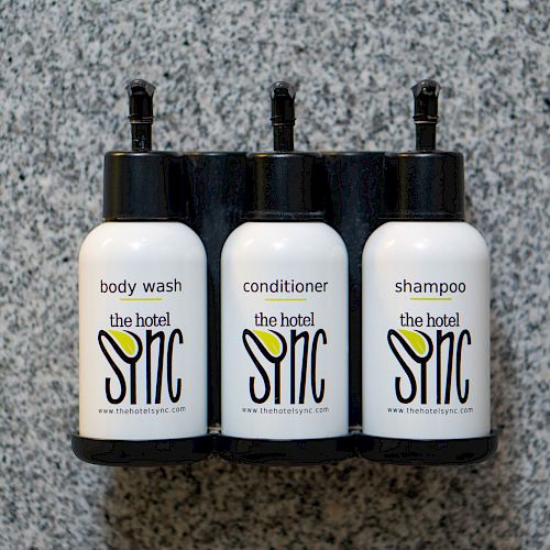 The image shows three mounted dispensers labeled as body wash, conditioner, and shampoo from 