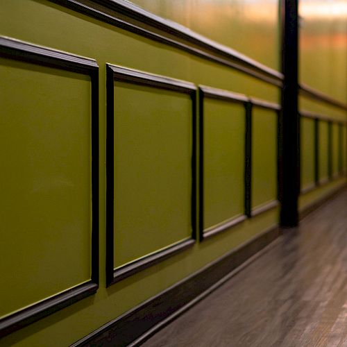 The image shows a hallway with green walls, decorative paneling, and a wooden floor leading to a lighted area at the end.