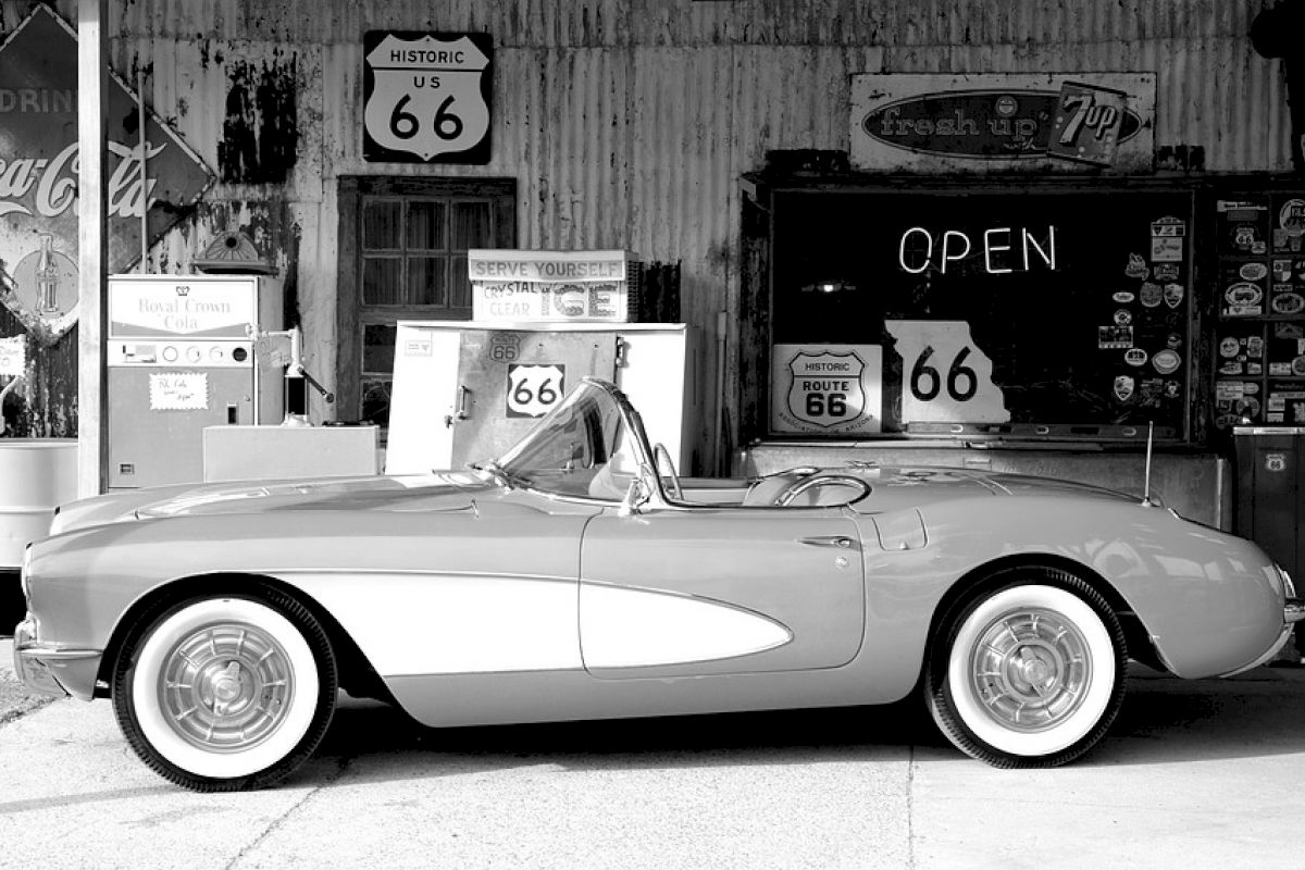 A classic car is parked in front of a vintage gas station with Route 66 signs and an 