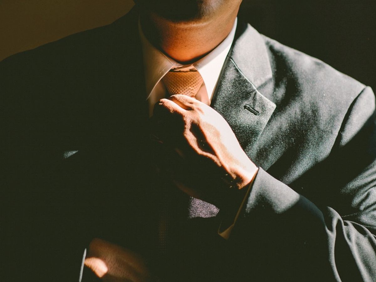 A person in a dark suit adjusts their tie, illuminated by soft lighting, creating a professional and sophisticated atmosphere.