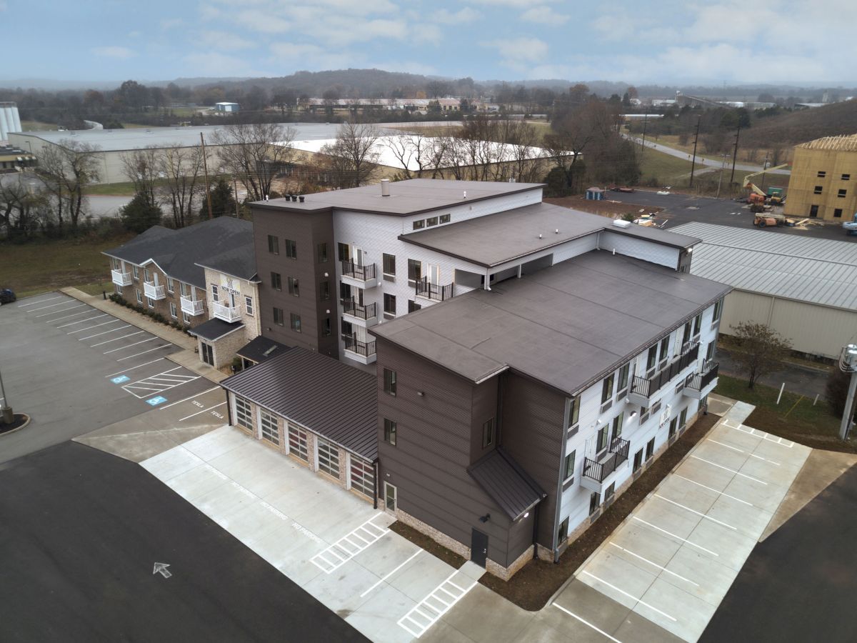 An aerial view of a multi-story building with parking areas and surrounding industrial structures and landscape under a cloudy sky.