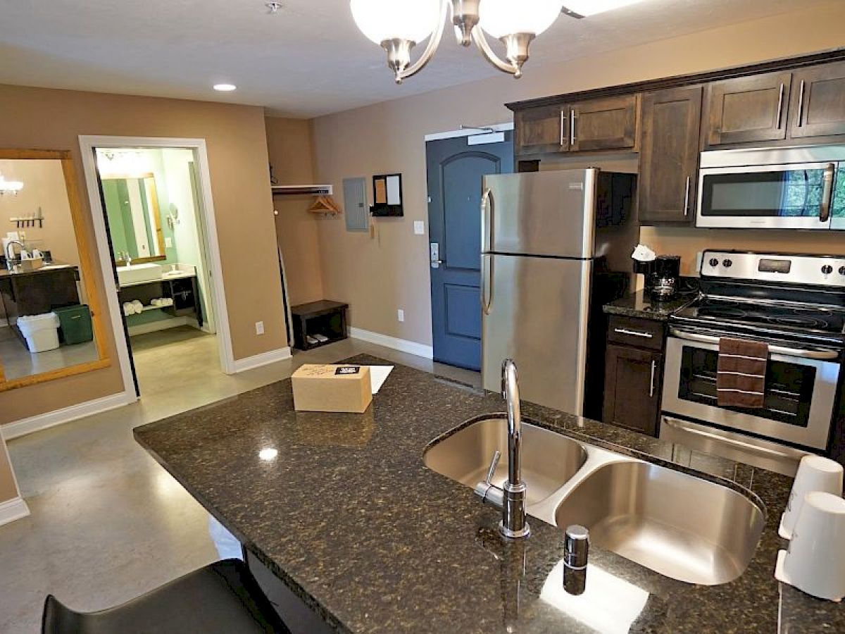 A modern kitchen features stainless steel appliances, dark wood cabinets, and a granite island. There's a glimpse of a bathroom and entryway area.