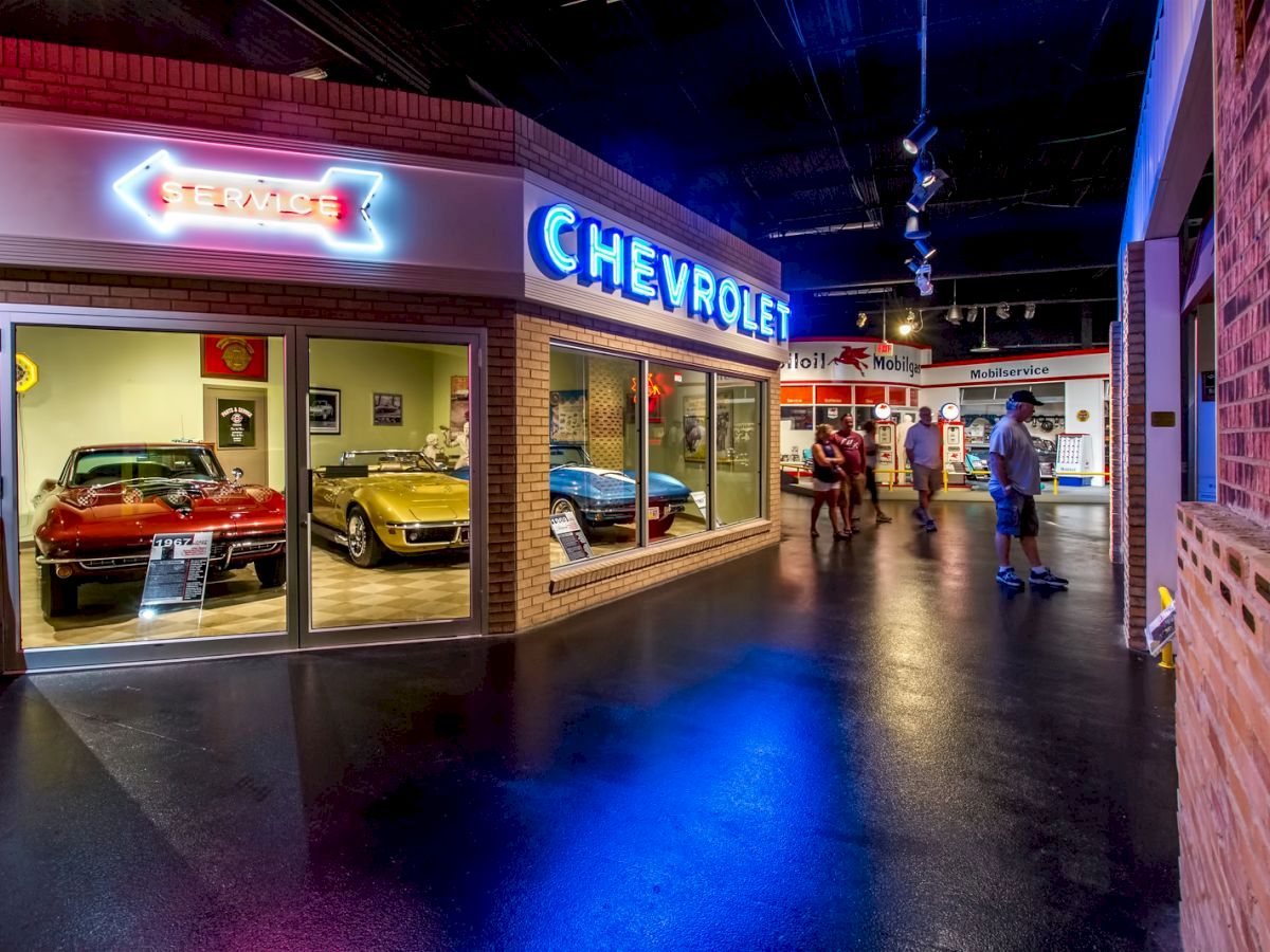 This image shows a museum exhibit with vintage Chevrolet cars on display, featuring neon signs and visitors walking through the space.