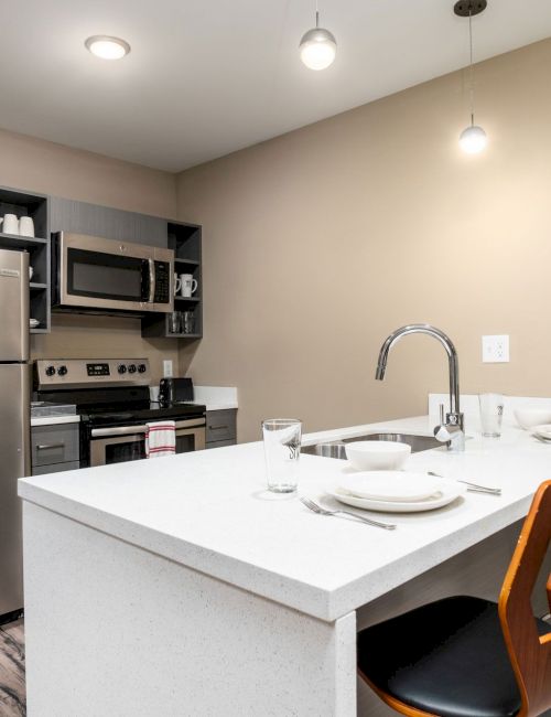 A modern kitchen features stainless steel appliances, an island with seating for two, and a neatly organized space with light fixtures.