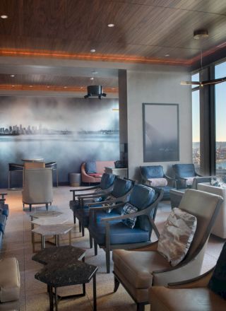 A modern lounge area with comfortable seating, large windows offering a scenic view of water and a Ferris wheel, and a cityscape mural on the wall.