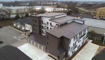 The image shows an aerial view of a multi-story building with adjacent parking spaces and nearby structures in a semi-rural area ending the sentence.