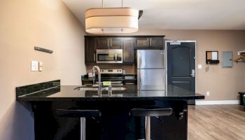 A modern kitchen with dark cabinets, stainless steel appliances, a black granite countertop island, and two bar stools.